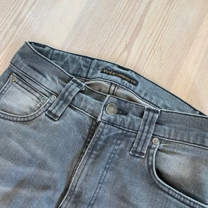Nudie Grå jeans  - Grå jeans från Nudie. Storlek W 25, L 30. Lite raka i benen. Har blivit fixade hos Nudie vid ena bakfickan, men stygnen är vara en cool detalj tycker jag. Säljer för 200 kr ☀️