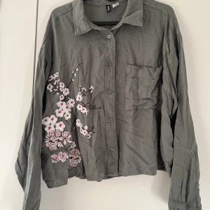 Skjorta - Kort skjorta med broderade blommor. Mer olivgrön på riktigt. Kan skickas