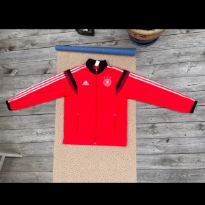 RARE Tyskland VM 2014 Track Suit Top - 2014 var ett stort år för tysk fotboll. Trots att CL tillhörde Madrid hade man fortfarande VM framför sig, där legender som Lahm, Klose och Schweini. Tyskland vann genom mål av Götze i finalen mot Argentina. Trackien har 3-4 fläckar och är M. (Ps 7-1)