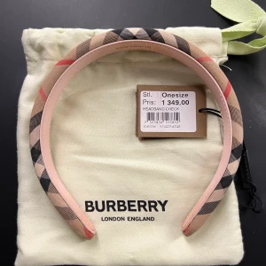 Burberry hårband/diadem - Ett hårband/diadem från Burberry, nästan oanvänt. Köptes på NK:S barnavdelning (men passar vuxna) förra sommaren för 1349kr, men har inte kommit till användning. Inga skador, missfärgningar eller smink på hårbandet. (Dustbagen ingår).❗️ Köparen står för frakten❗️