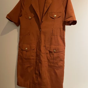 Klänning  - Roströd är färgen  Aldrig använd  Fina detaljer framtill 