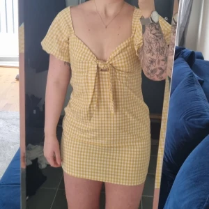 Klänning - En gul rutig klänning från nasty gal. Den har ballongärmar och ett gulligt snöre som går att knyta vid brösten. Jättesöt och passar perfekt på sommaren. Det står att klänningen är storlek 40 men den passar snarare en 36/38.