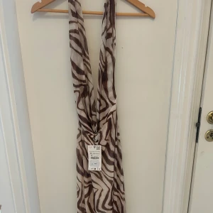 Zebramönstrad omlottklänning XS - Snygg omlottklänning i zebramönster med bruna och beige toner. Klänningen har djup v-ringning och är ärmlös, perfekt för dig som vill sticka ut. Lätt och luftig i materialet, passar till sommarens alla tillfällen.