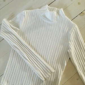 Vit ribbad polotröja från  Gina Tricot - Supersnygg vit ribbad polotröja från Gina Tricot. Tröjan har lång ärm, hög krage och är tillverkad i mjuk bomullsmix. Perfekt att styla med jeans eller kjol för en clean och fräsch look.