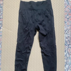 Träningstights med scrunch - Säljer dessa populära svarta seamless leggings med scrunch i rumpan och tight passform. De är tillverkade i ett stretchigt syntetmaterial som sitter skönt och formar sig efter kroppen. Perfekta för träning eller chill dagar. Inga synliga loggor eller mönster, bara clean och enkel stil.  Storlek L men passar ej mig som har L så skulle säga S/M. Aldrig använda.