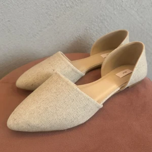 Beige ballerinaskor från Nelly - Helt nya endast testade stilrena ballerinaskor från Nelly i beige textil med spetsig tå och platt sula. Skorna har öppen insida och är tillverkade i ett linneliknande material som ger en naturlig och fräsch känsla. Perfekta för vår och sommar.