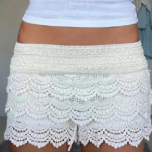Vita virkade spets-shorts - Superfina vita shorts med låg midja och flera lager virkad spets. De har ett elastiskt midjeband och ett detaljerat, romantiskt mönster med volangkant. Perfekta för sommarens varma dagar och ger en riktigt söt och bohemisk vibe.