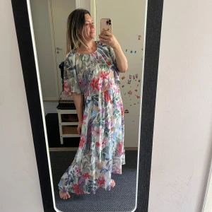 Blommig långklänning med vida ärmar - Superfin långklänning med blommigt mönster i rosa, lila, blått och grönt. Klänningen har vida, korta ärmar och en luftig passform. Perfekt för sommarens alla tillfällen! Tunt, flowy material och rund halsringning.Helt ny. Storlek passar både M och L