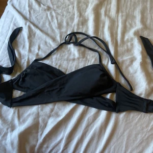 Svart bikiniöverdel från H&M med knyt - Snygg svart bikiniöverdel från H&M i storlek 36. Modellen har breda band som korsas framtill och knyts i nacken och ryggen för en cool och justerbar passform. Perfekt för stranden eller poolen.