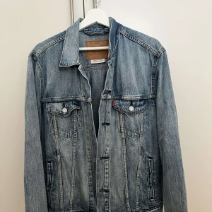 Klassisk jeansjacka från Levi's - Säljer en klassisk blå jeansjacka från Levi's med snygga sömmar och bröstfickor med knappar. Jackan har en tidlös design, krage och långa ärmar. Perfekt för dig som vill ha en ikonisk denimlook.