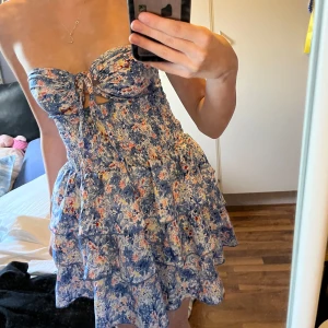 Blommig kort klänning med volanger - Supersöt kort klänning med blått och vitt blommönster, volanger och knytning framtill som man kan knyta på massa olika sätt, aldrig använd