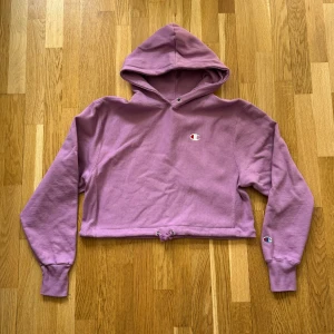 Dam Champion Lila Oversized Cropped Hoodie - Champion Oversized Cropped Hoodie med broderad logga på bröstet och armen i färgen lila till Dam.  Storlek: S, Armhåla till Armhåla: 54 cm, Längd: 48 cm, Axel till Armöppning: 63 cm.  Material: 82% Cotton, 18% Polyester.