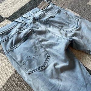 Replay Anbass ljusblå jeans - Säljer ett par Replay Anbass jeans i ljusblå tvätt. Klassisk femficksmodell med raka ben och snygga detaljer på bakfickorna. Jeansen är i stretchigt denim och har slim fit passform. Storlek W31 L32