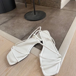 Vita strappy sandaler med fyrkantig tå - Snygga vita sandaler med tunna remmar och fyrkantig tå. Platt sula och minimalistisk design som ger en trendig look. Perfekta för varma dagar och lätta att matcha med sommarens outfits.