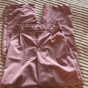 Rosa kostymbyxor från H&M Divided - Snygga ljusrosa kostymbyxor från H&M Divided i storlek XXS. Byxorna har hög midja, raka ben och stängs med dragkedja och hake. Tillverkade i en mjuk blandning av viskos, polyester och elastan för en bekväm passform.