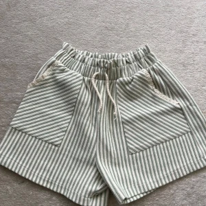 Randiga shorts från Zara med spets - Superfina shorts från Zara i vitt och ljusgrönt med smala ränder. De har elastisk midja med snörning, stora fickor framtill och söt spetsdetalj vid fickorna. Perfekta för varma dagar och riktigt sköna att ha på sig.