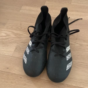 Svarta adidas fotbollsskor med lång strumpa och bra skick  - Snygga svarta fotbollsskor från adidas med vita detaljer och grafiskt mönster på de klassiska tre ränderna. Skorna har snörning och dobbar för bra grepp på planen. Ovandelen är i syntetmaterial och designen är modern med rund tå.