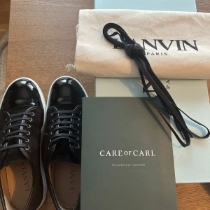 Svarta Lanvins (helt oanvända) - svarta sneakers från Lanvin med ovandel i mocka och lackad tå. Size uk 8 dvs storlek 42/43. Skorna har vita platta sulor och svarta skosnören. Skorna har används 1 gång varpå därför jag ej får returnera dem. Dem är helt ny som ni ser på bilderna och kostar nypris 4999kr mitt pris 3800kr!!! Kvitto samt box och allt medföljer, dem är köpta från careofcarl
