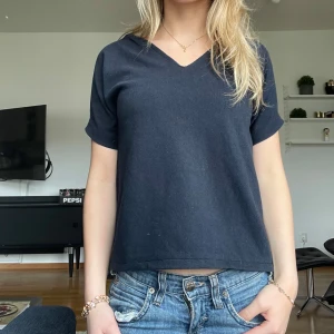 Mörkblå v-ringad t-shirt - En stilren mörkblå t-shirt med v-ringning och korta ärmar. Modellen är rak och något loose fit, vilket ger en avslappnad vibe. T-shirten är i ett mjukt bomullstyg som känns skönt mot huden. Perfekt till jeans eller shorts för en enkel och snygg look.