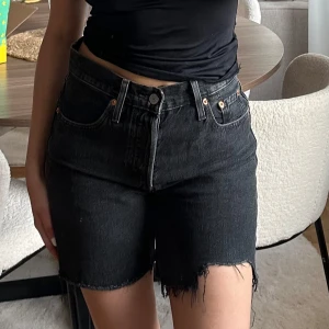 Svarta jeansshorts från Levi's - Säljer ett par svarta jeansshorts från Levi's med råa, fransiga benslut och klassisk femficksdesign. Shortsen har hög midja och är tillverkade i kraftig denim. Perfekta för en avslappnad och cool look. Storlek W25