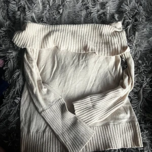 Offshoulder beige tröja BCBG Max Azria - Superfin beige offshoulder-tröja från BCBG Max Azria. Tröjan har bred ribbad kant upptill och vid ärmslut samt nederkant, vilket ger en snygg och trendig look. Perfekt för dig som gillar stilrena och mjuka plagg med lite extra detalj.