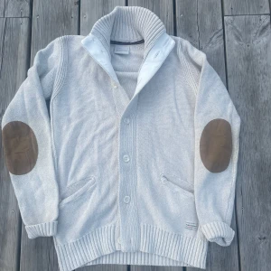 stickad kofta med mockadetaljer - Cool kofta från Peak performance. Perfekt till sommarkvällar! Koftan har ribbad krage, muddar och nederkant samt knäppning framtill med fyra knappar. Två fickor framtill och en chill, klassisk look. 