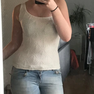 Vit broderad linnetopp - Säljer en vit linnetopp med broderat blommönster och ärmlös design. Toppen har en rundad halsringning och sitter tajt mot kroppen. Perfekt för varma dagar och enkel att matcha med jeans eller kjol.