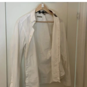 Vit Burberry Brit skjorta med rutiga detaljer - Vit skjorta från Burberry Brit med klassiska rutiga detaljer i krage och ärmslut. Skjortan har lång ärm, knappar framtill och är tillverkad i bomull. Snygg och stilren modell med exklusiv känsla och ikoniska Burberry-rutor som sticker ut.