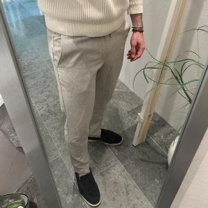 Beige byxor  - Snygga beige byxor och diskret fiskbensmönster. Byxorna har resår och snörning vid benslut samt fickor på sidorna och bak. Perfekta för en chill och stilren look.