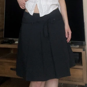 Svart kjol med bälte från KappAhl - Svart, midikjol från KappAhl med snyggt bälte i midjan och markerade veck. Kjolen har en klassisk A-linjeform och är perfekt för dig som gillar stilrena och enkla plagg. Passar till många olika looks och är lätt att matcha.