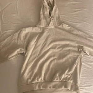 Beige hoodie med huva och snörning - En stilren beige hoodie med huva och snörning. Tröjan har långa ärmar och bred mudd nertill för en skön passform. Perfekt för dig som gillar en enkel och clean look. Materialet känns mjukt och passar året runt. Är mer som storlek S men är M