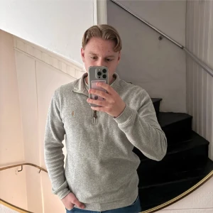 Grå half zip från Polo Ralph Lauren - Säljer en stilren grå långärmad tröja från Polo Ralph Lauren med half zip och broderad logga på bröstet. Tröjan har en klassisk passform och är tillverkad i mjuk bomullsmix, perfekt för lager-på-lager under höst och vinter.
