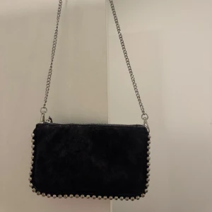 Svart väska från Zara - Snygg svart axelväska i mocka med silverfärgad kedjerem och nitar runt hela kanten. Axelbandet går att ta av om man skulle vilja ha det som en handväska! Basic men extra, passar perfekt till olika outfits✨✨