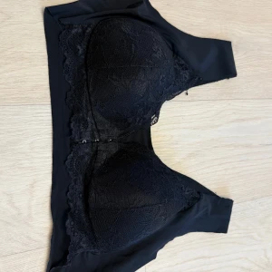 Svart spetsig korsett-topp - Supersnygg svart korsett-topp med vadderade kupor och spetsdetaljer framtill. Toppen har en croppad passform och knäppning framtill. Perfekt för att lyfta vilken outfit som helst med en edgy vibe.