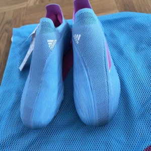 Adidas X Speedflow+ FG blå fotbollsskor - Säljer ett par Adidas X Speedflow+ FG fotbollsskor i en fräsch ljusblå färg med rosa detaljer. Skorna har en strömlinjeformad design utan snörning, mesh-överdel och rosa dobbar för bästa grepp på planen. Perfekta för dig som vill sticka ut på matchen.