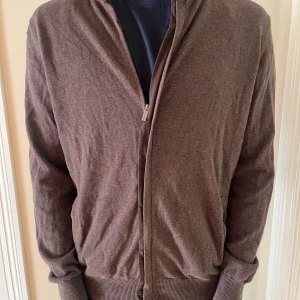 Brun cardigan jacka i kashmir - Mjuk brun cardigan jacka från Ermenegildo Zegna i lyxig kashmir. Jackan har dragkedja framtill, ribbade muddar och en klassisk, avslappnad passform. Perfekt för dig som gillar stilren och bekväm look.