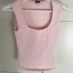 Ljusrosa ribbad linnetopp Gina Tricot XS - Supersöt ljusrosa ribbad linnetopp från Gina Tricot i storlek XS. Toppen har en djup rundad urringning med liten rosett framtill och ärmlös design. Perfekt för en söt och enkel look, lätt att matcha med jeans eller kjol. Aldrig använd!!