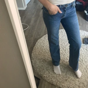 Blå raka jeans med fickdetaljer - Säljer ett par klassiska blå jeans med raka ben/ bootcut och snygga fickor med knappdetaljer bak. Jeansen har normal midja och stängs med knapp och dragkedja. Perfekta för dig som gillar en tidlös och avslappnad look. Dem är storlek S full alltså passar dem folk med lite längre ben. Jag är 176-175 ungefär som referens. Säljer då dem inte kommer till användning. Knappt använda. Köpte för 300.