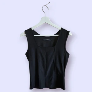 Svart linnetopp från One Two - Snygg svart linnetopp från One Two med breda axelband och markerade sömmar framtill som ger en cool och stilren look. Perfekt att matcha med jeans eller kjol för en trendig outfit.