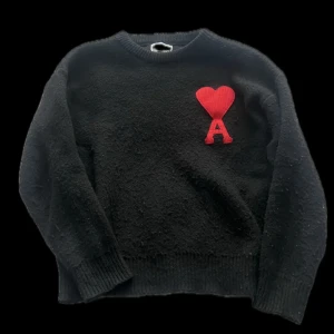 Svart stickad tröja från Ami Paris - Svart stickad tröja från Ami Paris med rund hals och lång ärm. På bröstet finns ett rött hjärta med bokstaven A, vilket ger en unik och trendig look. 