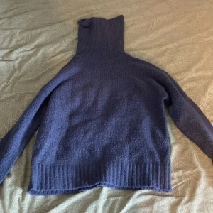 Mörkblå stickad polotröja - Mysig mörkblå stickad polotröja med hög krage och långa ärmar. Perfekt för kalla dagar när du vill ha något både snyggt och bekvämt. Tröjan har ribbade muddar och en klassisk, enkel design som funkar till det mesta.