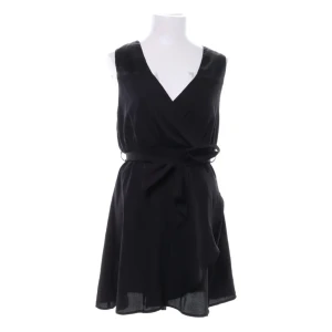 Svart omlottklänning Rut&Circle - Svart omlottklänning från Rut&Circle. Klänningen är ärmlös, har v-ringning och knyts i midjan med ett bälte för en snygg siluett. Perfekt för dig som gillar stilrena och enkla plagg med en modern touch. Sval och skön nu i sommar.