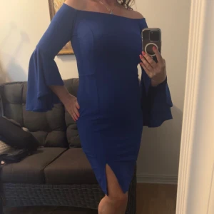 Kornblå offshoulder klänning med volangärm - Supersnygg kornblå klänning med offshoulder och vida volangärmar. Figurnära passform och slits framtill för extra edge. Perfekt för dig som vill sticka ut med en cool och elegant look.