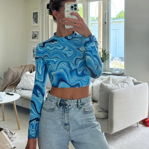 Blå croppad topp med vågmönster Shein - Säljer en croppad långärmad topp från Shein med blått vågmönster i olika nyanser. Toppen har en tight passform och är gjord i ett stretchigt syntetmaterial. Perfekt för dig som gillar färg och vill sticka ut lite extra.