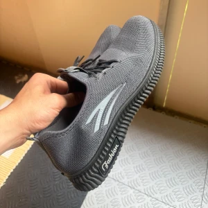 Grå sneakers med stickad ovandel - Snygga grå sneakers från Vogue Fashion med stickad ovandel och svarta detaljer. Skorna har snörning, rund tå och en rejäl, räfflad sula för extra grepp. Perfekta för dig som gillar en clean och sportig look.