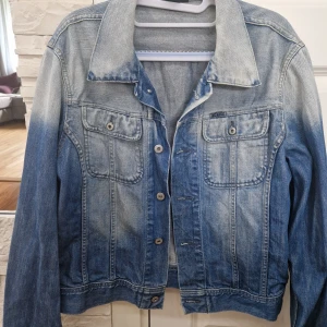 Blå jeansjacka från Diesel, stl M - Snygg blå jeansjacka från Diesel i klassisk modell med två bröstfickor och knappar framtill. Jackan har en cool tvättad look och är tillverkad i slitstarkt denim. Perfekt för dig som vill ha en tidlös och trendig jacka till din garderob.