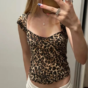Leopardmönstrad croppad topp - Snygg croppad topp med leopardmönster och korta ärmar. Toppens passform är tight och den har en lätt v-ringad halsringning. Perfekt för dig som vill sticka ut med ett djurmönster och en trendig look.