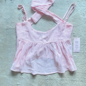 Ljusrosa flowy topp med rosett Nelly - Supersöt ljusrosa flowy topp från Nelly med smala axelband och stor knytbar rosett i ryggen. Helt ny endast testad lite för stor på mig tyvärr därav att jag säljer den! Str S 