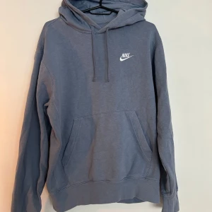Blå hoodie från Nike med huva - Säljer en blå hoodie från Nike i storlek XS. Tröjan har huva med snörning, stor magficka och Nike-logga broderad på bröstet. 