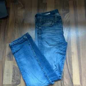 Blå slim fit jeans Jack & Jones - Snygga blå jeans från Jack & Jones i modellen Glenn med slim fit-passform. Klassisk femficksdesign, normal midja och lätt slitningar för en cool look. Finns 2 små hål på undersidan (sista bilden) ett hål är igenlappat med jeanstyg. Hålen synnd knappt när man står upp